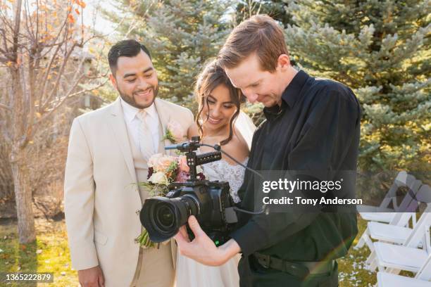 bride and groom working with camera operator at outdoor wedding - photographer stock pictures, royalty-free photos & images