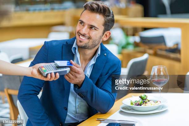 a closeup shot of a businessman using his contactless card for a payment, while having lunch in a restaurant - customers pay with contactless cards imagens e fotografias de stock