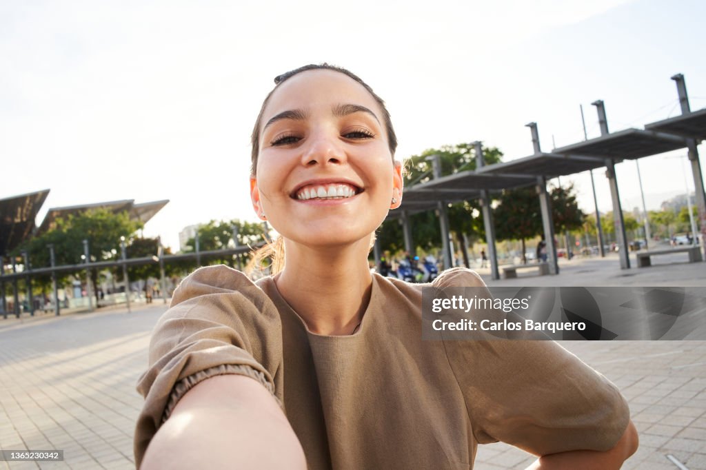 Cheerful portrait of a Caucasian lady taking a selfie outdoors.