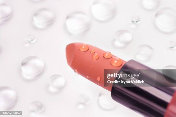 moisturizing lipstick in peach color and drops of water or beauty cosmetic product essential oil  on  pastel gray color background. - damp lips stock-fotos und bilder