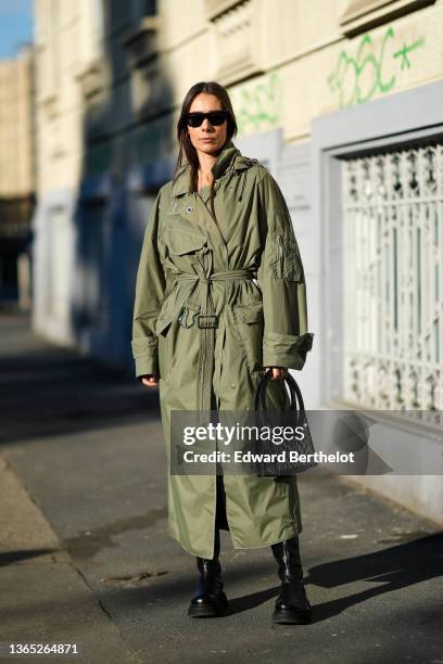 Alice Barbier wears sunglasses, a green khaki long trench coat, black leather shoes, outside the K-way fashion show, during the Milan Men's Fashion...