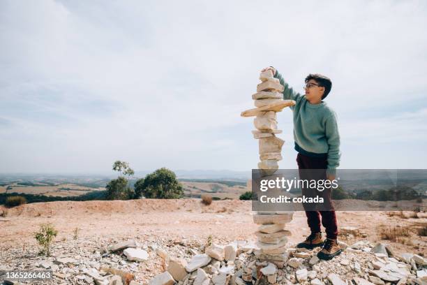 boy building large rock totem - totem imagens e fotografias de stock