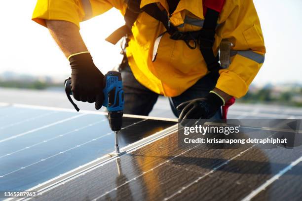 male technician in yellowsuit installing photovoltaic blue solar modules with screw. man electrician panel sun sustainable resources renewable energy source alternative innovation - control panel stock-fotos und bilder