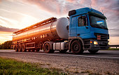 A blue modern truck with a semi-trailer tanker transports dangerous goods against the backdrop of the evening sunset. The concept of transportation of liquid cargo, hazard class ADR. Industry