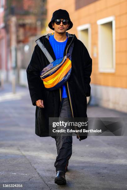 Rahi Chadda wears a black velvet bob / hat, black sunglasses, a royal blue electric braided wool pullover, a black hoodie oversized long zipper coat,...