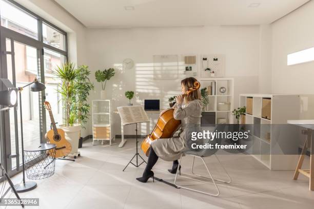 vue arrière d’une femme assise et jouant du violoncelle en studio - pupitre à musique photos et images de collection