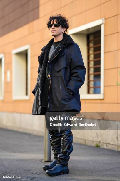 Guest wears black sunglasses, a black leather t-shirt, gold earrings, a black oversized with black sheep collar long coat from K-way, black shiny...