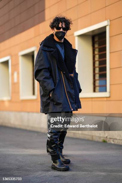 Guest wears black sunglasses, a black leather t-shirt, gold earrings, a black oversized with black sheep collar long coat from K-way, black shiny...