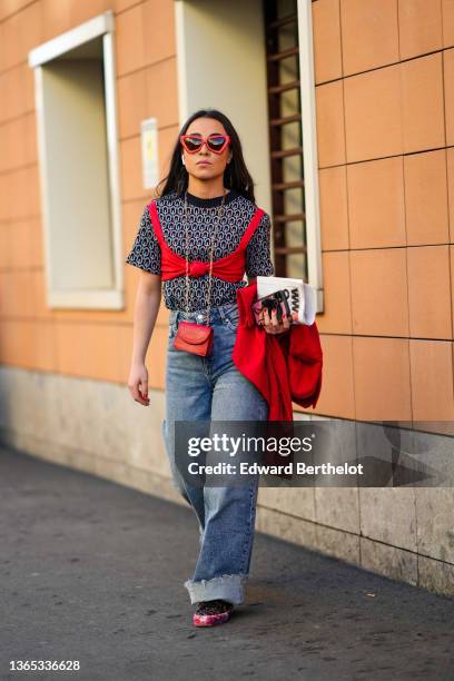 Guest wears red sunglasses, a black with pale gray and red print pattern short sleeves t-shirt, a red knot bra under-wear, a red shiny leather...