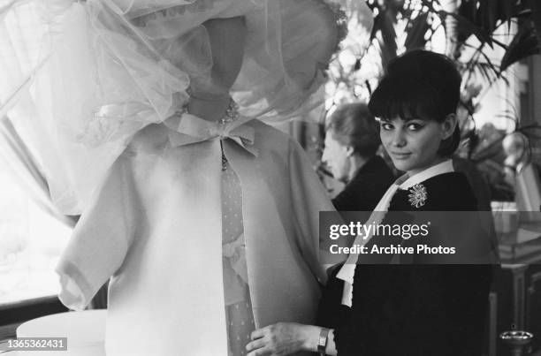 Tunisian-born Italian actress Claudia Cardinale admires an outfit on a mannequin, circa 1960.