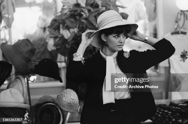 Tunisian-born Italian actress Claudia Cardinale tries on a hat, circa 1960.