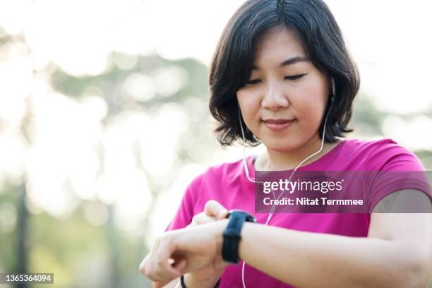 track workouts and activities on smartwatch. asian female runner in sportswear checking smart watch to track her steps and heart rate variability after jogging. - 心臓刺激伝導系 ストックフォトと画像