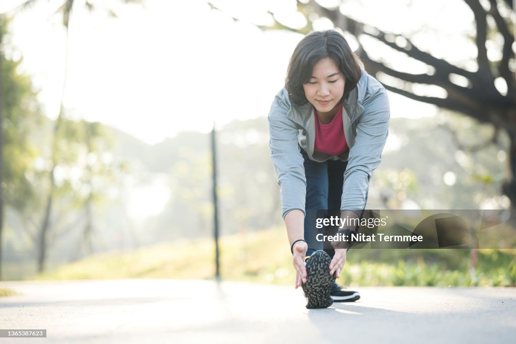 Stretching may decrease your risk of injury during workout. Asian female runner doing leg stretch before morning jogging on trails in city park.