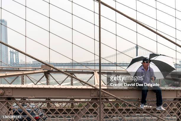 Man sits on the Brooklyn Bridge as smoke from wildfires in Canada shrouds lower Manhattan on June 30, 2023 in New York City. The eastern U.S. Is once...
