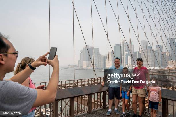 Family poses for a photo on the Brooklyn Bridge as smoke from wildfires in Canada shrouds lower Manhattan on June 30, 2023 in New York City. The...