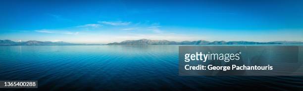 long panorama of calm sea and mountains in the background - greece sea stock pictures, royalty-free photos & images