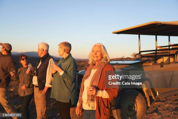 carefree senior woman on safari drinking champagne at sunset - südafrika safari stock-fotos und bilder