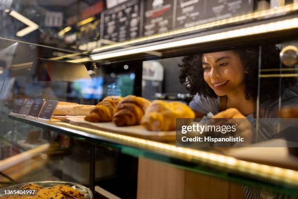 happy waitress working at a cafe and placing pastries in the counter display - boulangerie vitrine stockfoto's en -beelden