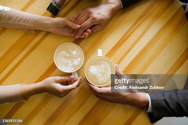 a man and a woman holding hands in a cafe, drinking coffee. lovers' hands on the background of a wooden table. breakfast or lunch at the restaurant. engagement, a guy holding his girlfriend's hand tightly. romantic meeting, valentine's day. - coppie cibo food bistrot foto e immagini stock