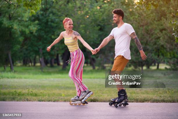 side view of a woman and a man holding hands while roller-skating - inline skating man park stock pictures, royalty-free photos & images