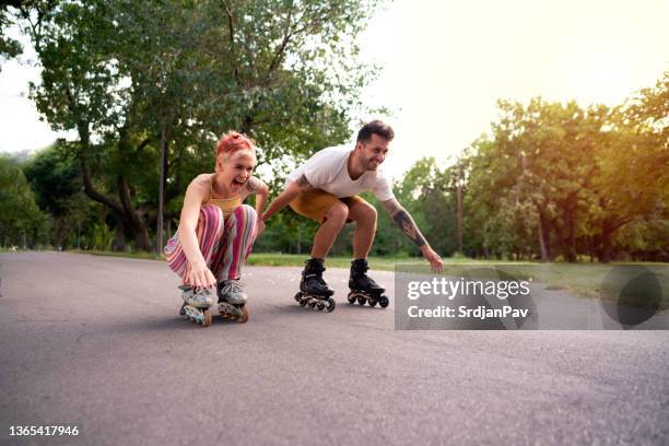happy woman and man having fun on roller skates - rolschaatsen schaats stockfoto's en -beelden