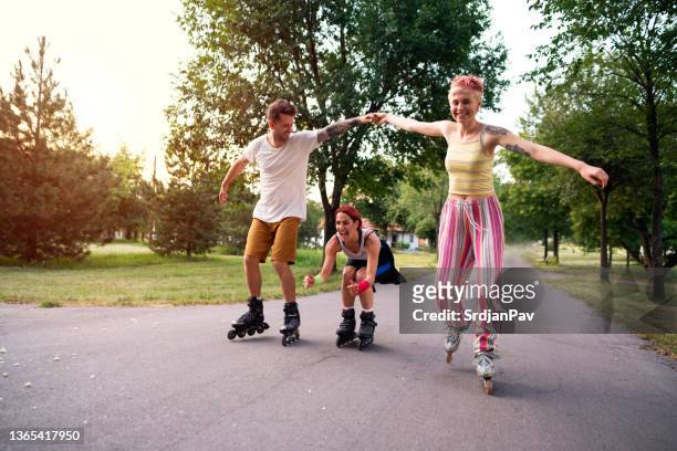 amigos sonrientes divirtiéndose patinando sobre ruedas en el parque - patín en línea fotografías e imágenes de stock