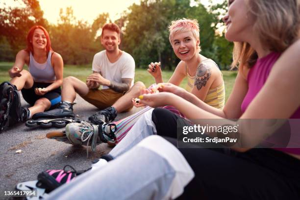 glückliche junge leute sitzen beim gemeinsamen popcornessen im freien - snacks stock-fotos und bilder