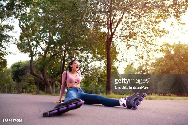 joven patinadora riendo mientras está sentada en la carretera después de la caída - patín en línea fotografías e imágenes de stock