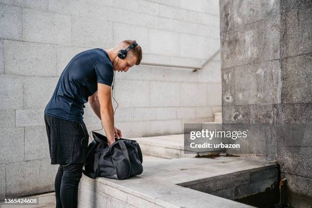 young man packing a gym bag after a workout - gym bag stock pictures, royalty-free photos & images