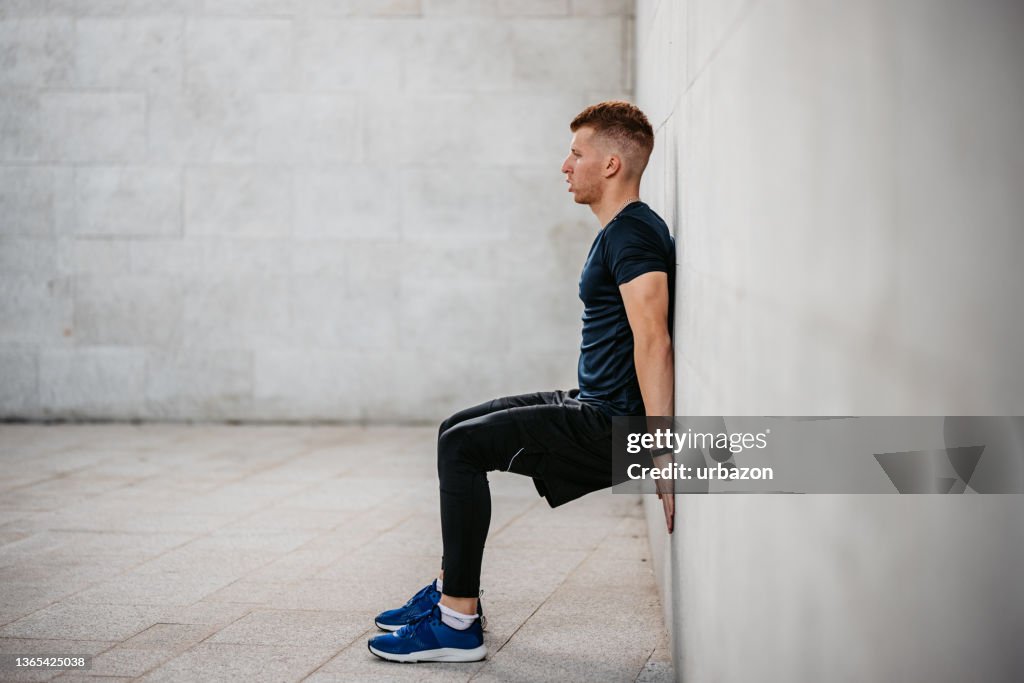 Young Man Doing The Wall Sit Exercise Outdoors