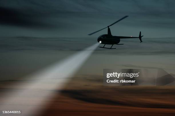 helicopter flight shining spotlight beam in dark sky - military helicopter stock-fotos und bilder