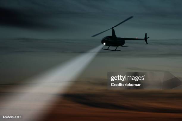 helicopter flight shining spotlight beam in dark sky - hélicoptère ville photos et images de collection