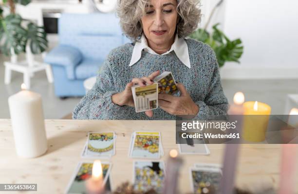 senior woman reading tarot cards on table at home - tarocchi foto e immagini stock