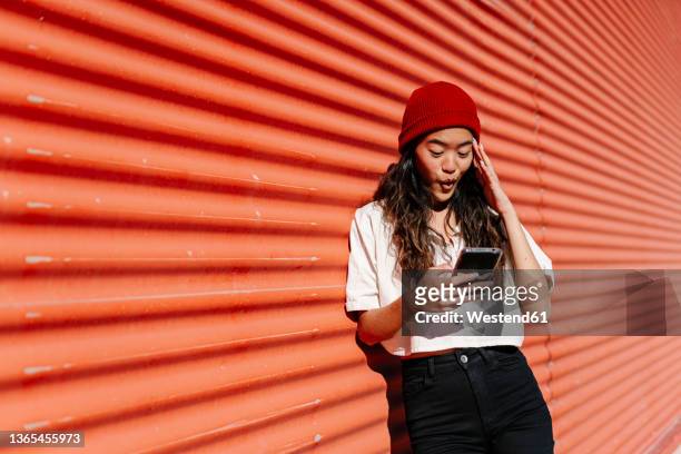 surprised woman using mobile phone in front of corrugated wall - frau staunen stock-fotos und bilder