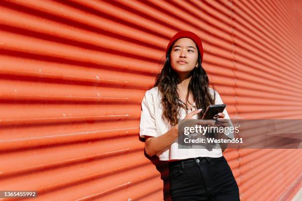 thoughtful woman holding smart phone at wall - young women stock pictures, royalty-free photos & images