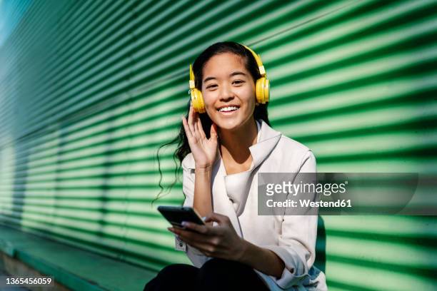 young woman with headphones and mobile phone in front of wall - headphones asian fotografías e imágenes de stock