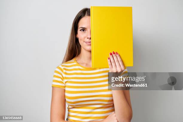 woman covering face with yellow book against gray background - buch freisteller stock-fotos und bilder
