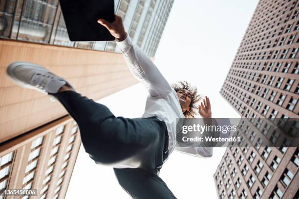 excited businessman holding digital tablet jumping amidst office buildings - low angle view stock pictures, royalty-free photos & images