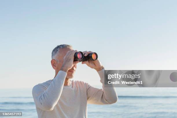 man looking through binoculars at beach - binoculars imagens e fotografias de stock