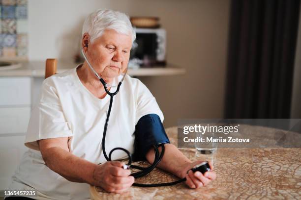 an old sick woman self-medicates; measures pressure on herself in the kitchen - stroke illness stock pictures, royalty-free photos & images