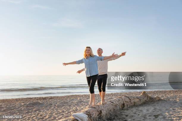 couple with arms outstretched walking on tree log at beach - balance copy space stock pictures, royalty-free photos & images