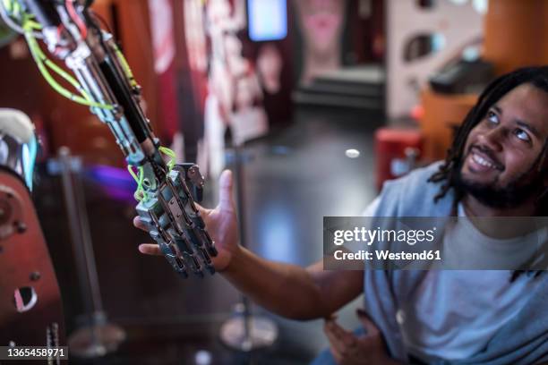 young tech developer shaking hand with robotic arm at workshop - robot hand shake stock pictures, royalty-free photos & images
