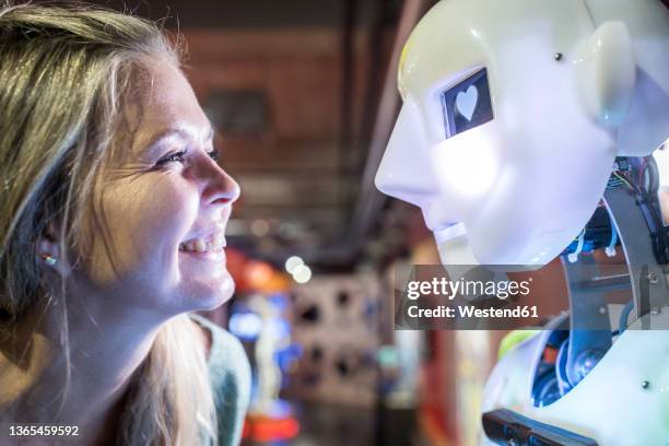 happy technician looking at human robot with heart shape in eye - robotic heart stock-fotos und bilder