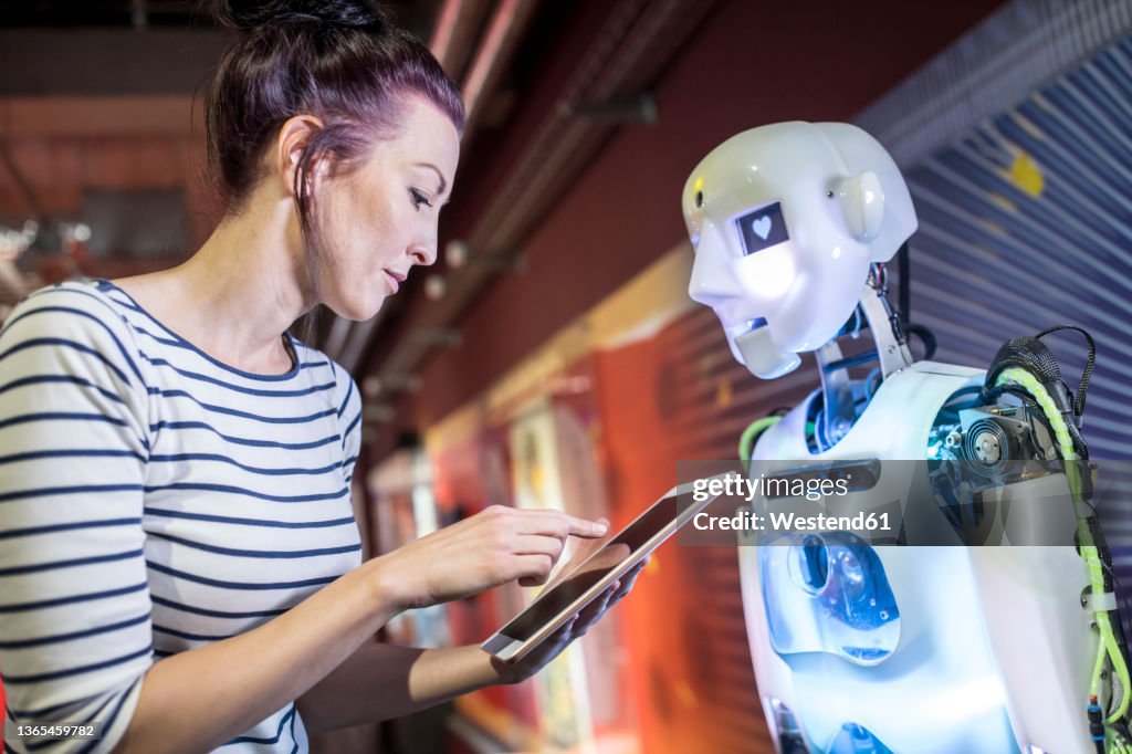Technician programming human robot through tablet PC at workshop