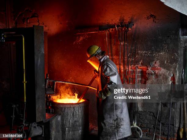foundry worker wearing protective suit burning in furnace at metal industry - steel mill stock-fotos und bilder