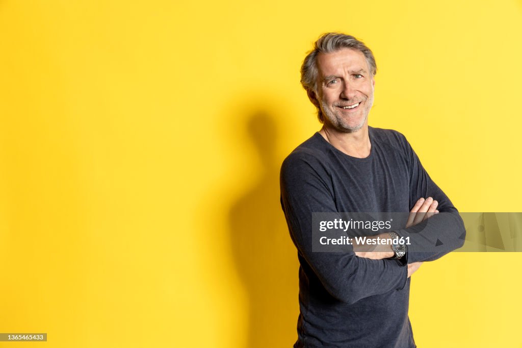 Smiling businessman with arms crossed in front of yellow background