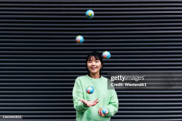 woman juggling with globe balls in front of black corrugated wall - fare il giocoliere foto e immagini stock