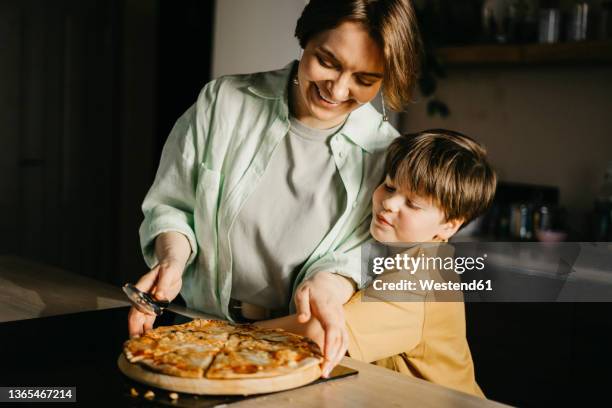 son embracing mother holding pizza and cutter at home - ピザカッター ストックフォトと画像