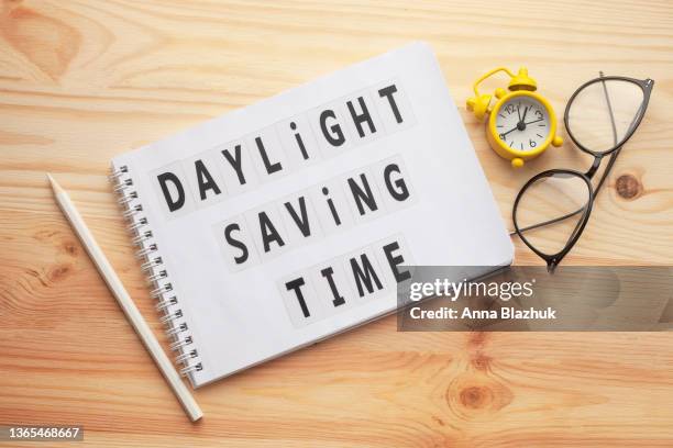 daylight saving time, notepad with text and retro alarm clock on wooden table. - spring forward fotografías e imágenes de stock