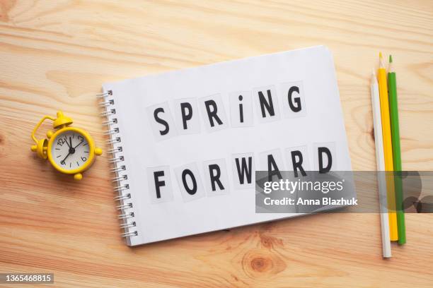 daylight saving time, notepad with text spring forward and retro alarm clock on wooden table. - daylight saving time foto e immagini stock